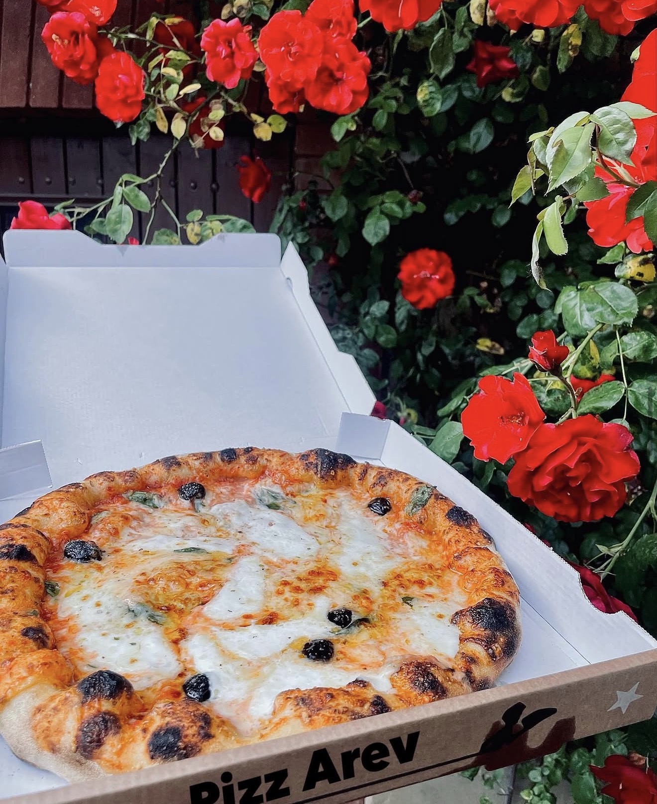 Pizza Pizz’Arev dans sa boîte, présentée devant des roses